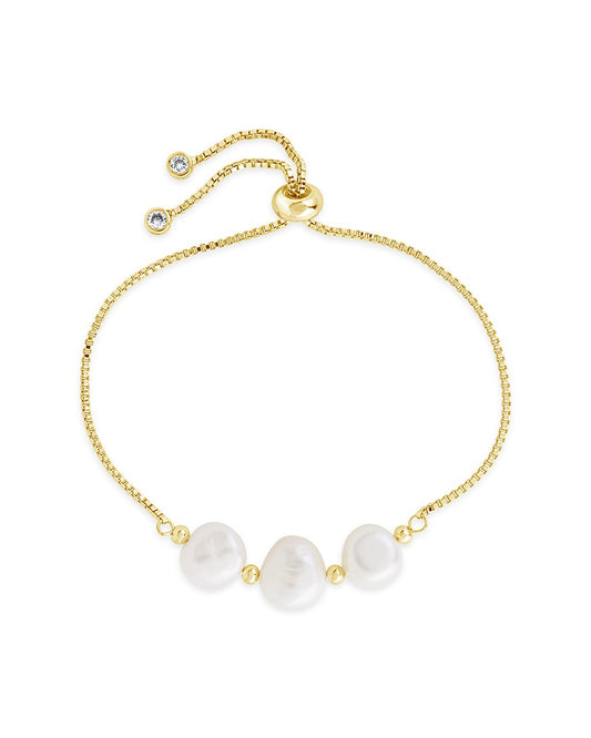 A gold-tone bracelet featuring three white pearls and a sliding knot closure, presented on a white background.