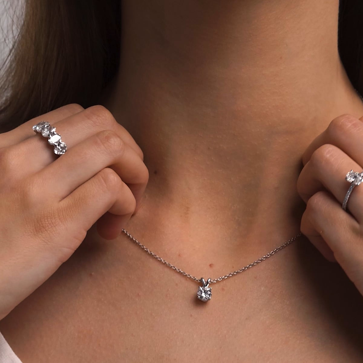 Person wearing a silver necklace with a pendant, close-up of the necklace and rings.